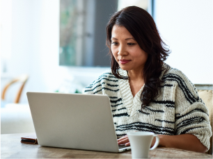 Asian pacific islander woman working at a table at home with a laptop and coffee