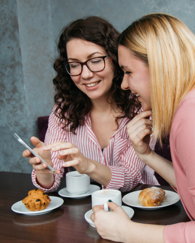 Two women at coffee shop looking at phone