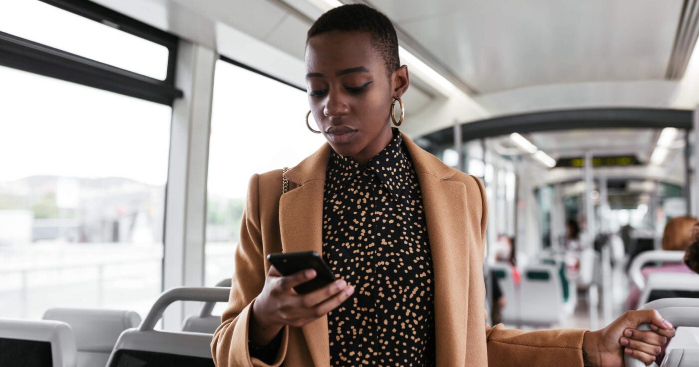 Stock image photo of black woman holding mobile phone on train
