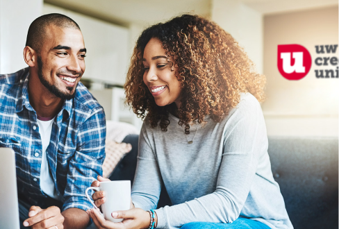 Black man and woman sitting in front of computer with a coffee mug and the University of Wisconsin Credit Union Logo behind them