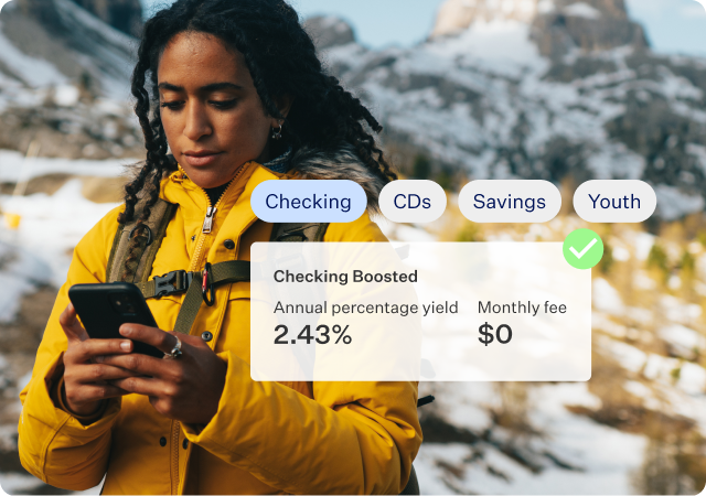 Image of woman in a yellow winter coat and a backpack in the snowy mountains on her phone. With an overlay of a section of product screen showing the different deposit accounts that she has— Checking ,CDs, Savings and Youth.