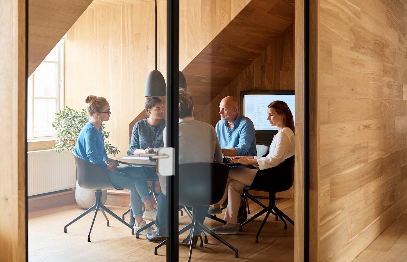 Business people discussing in meeting seen through glass door at office.